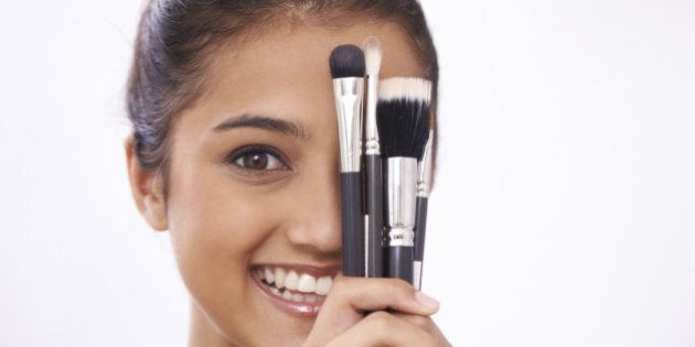 A young woman holding makeup brushes against her face