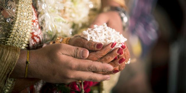 This is a Ritual in the Hindu Weddings, where 'puffed Maize gains'(Khoi) are given to the Fire God by the bride and Groom. The Fire God is considered the Witness to the marriage and is worshiped during the Marriage Rituals.Here you can see the hands of the bride and groom ready to make the offering to the Fire God.
