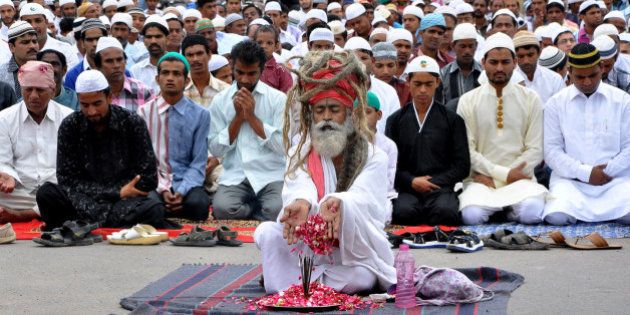 An Indian Hindu Sadhu performs an act of worship while Muslims offer Eid-ul-Fitr prayers at Jalori Gate in Jodhpur on August 9, 2013. Muslims around the world are celebrating Eid al-Fitr, which marks the end of the fasting month of Ramadan AFP PHOTO/STR (Photo credit should read STRDEL/AFP/Getty Images)