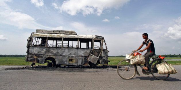 A man rides a bicycle in front of a bus that was burnt by a mob on the national highway near Rongia town in the northeastern Indian state of Assam August 16, 2012. Fresh violence flared in previously calm areas of Assam on Thursday, with a hundreds-strong mob burning a bus and a wooden bridge in apparent retaliation for a similar attack on a car, officials said. REUTERS/Utpal Baruah (INDIA - Tags: CIVIL UNREST POLITICS TPX IMAGES OF THE DAY)