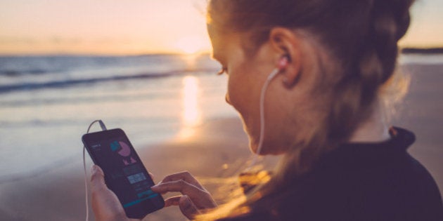 Woman using self tracking app on her smartphone after running at the beach.