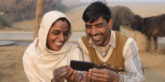 India, Uttar Pradesh, Agra, husband and wife looking at smart phone in rural setting.