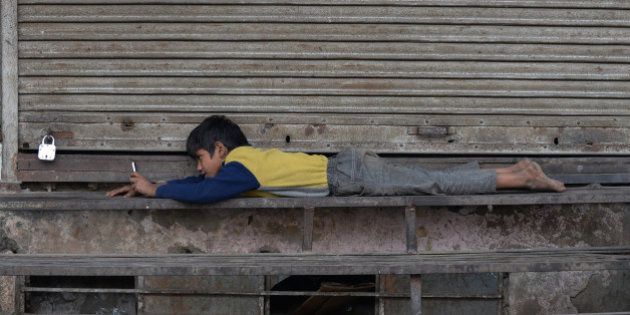 An Indian street child uses a cellphone outside a closed shop in New Delhi on December 7, 2015. AFP PHOTO/ SAJJAD HUSSAIN / AFP / SAJJAD HUSSAIN (Photo credit should read SAJJAD HUSSAIN/AFP/Getty Images)