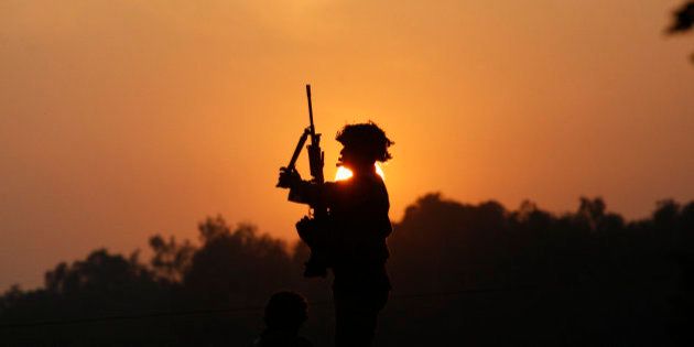 An Indian army soldier is silhouetted against the setting sun as he stands guard next to his colleague, sitting on the roof top of a house outside the Indian air force base in Pathankot, India, Sunday, Jan. 3, 2016. Indian troops were still battling at least two gunmen Sunday evening at the air force base near the country's border with Pakistan, more than 36 hours after the compound came under attack, a top government official said. (AP Photo/Channi Anand)