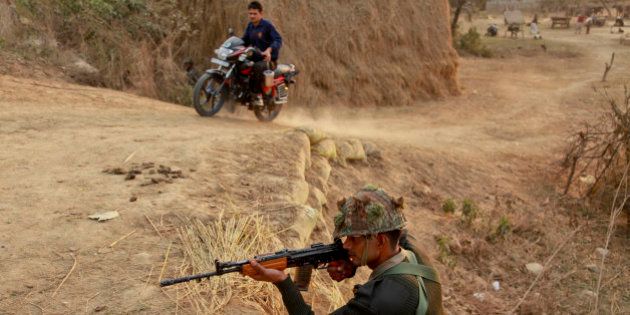 An Indian civilian rides past as an army soldier takes position outside the Indian air force base in Pathankot, India, Sunday, Jan. 3, 2016. Indian troops were still battling at least two gunmen Sunday evening at the air force base near the country's border with Pakistan, more than 36 hours after the compound came under attack, a top government official said. (AP Photo/Channi Anand)