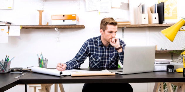 A young creative ponders his work projects whilst sitting at his desk at the office