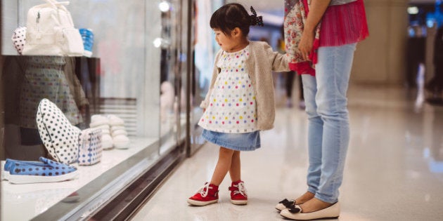 Lovely little girl holding hands with her mom while looking at the shopping window display in the shopping mall joyfully