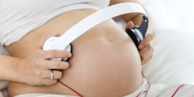 Portrait of pregnant woman putting headphones on her belly.