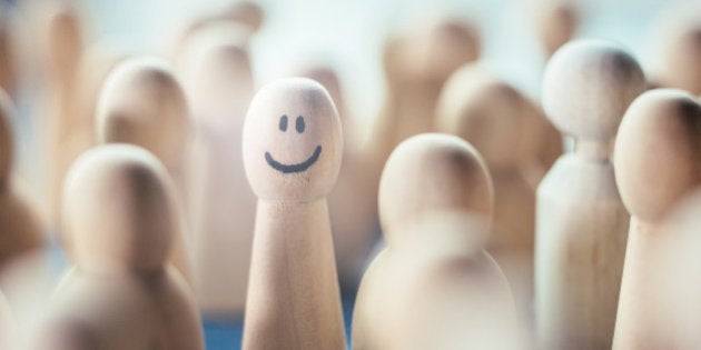 Happy pawn figure in a group of faceless pawns, close-up.