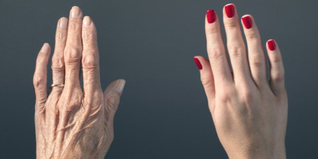 Studio photograph of elderly woman's hand beside a younger woman's hand.
