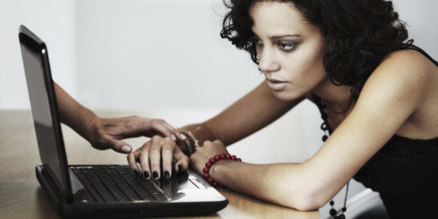 A young woman looking at her laptop while a hand is coming out of the screen to touch her on the arm