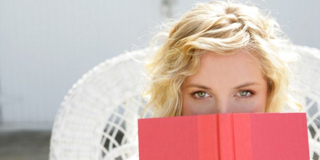 Young woman peeking over open book.