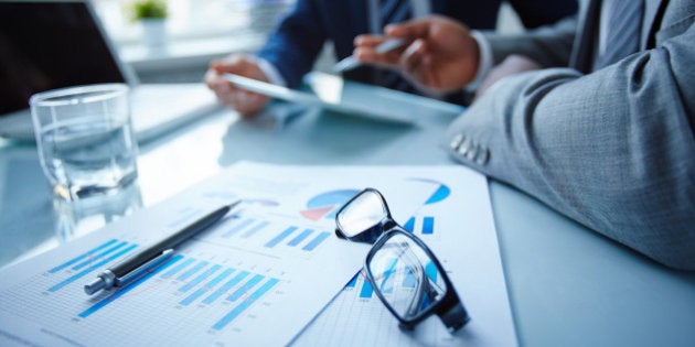 Image of eyeglasses and financial documents at workplace with businessmen discussing ideas near by