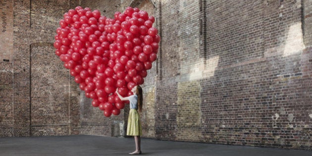 Woman in empty warehouse hugging red heart made of balloons