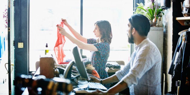 Clothing store owners sorting inventory behind counter in vintage clothing shop