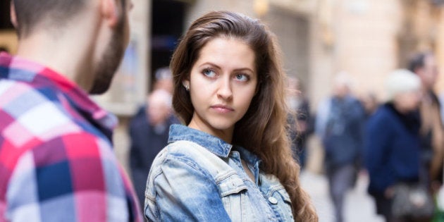 Couple having a quarrel on a city street. Woman is standing half-turned to her boyfriend with a dissapointed look on her beautiful face
