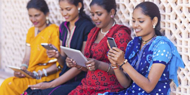 Four indian women playing with digital tablets and smart phones.
