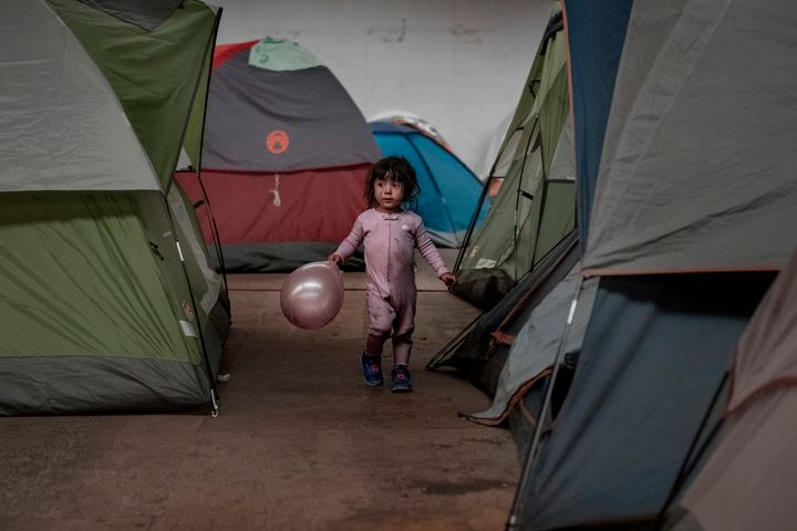 A girl holds walks among tents inside an empty warehouse used as a shelter set up for migrants in downtown Tijuana, Mexico.