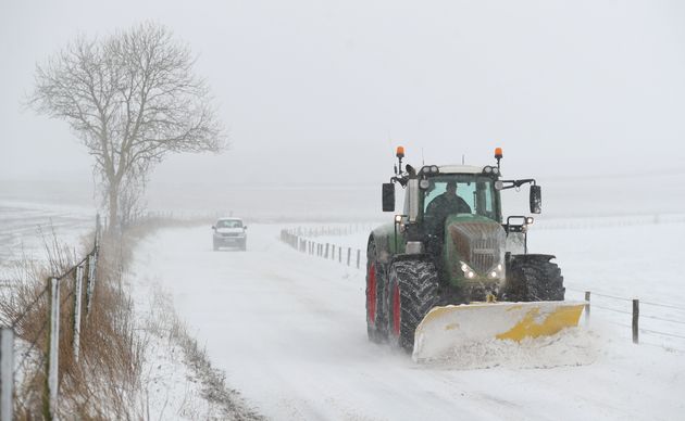 A tractor with a snow plough clears the snow on the B3081 near to Shaftesbury in Dorset 