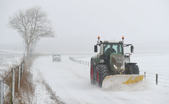 A tractor with a snow plough clears the snow on the B3081 near to Shaftesbury in Dorset 