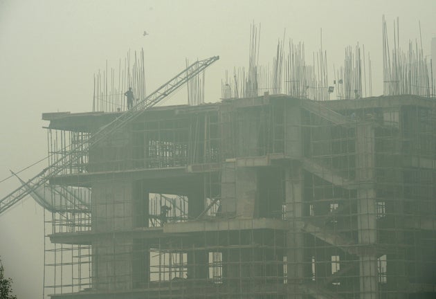 File photo of labourers working in an under-construction building as smog covers the capital's skyline...