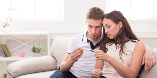 Sad couple after negative pregnancy test result, sitting on couch at home, copy space