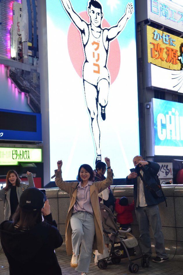 グリコの看板の前でポーズを決めて写真を撮る観光客ら＝4月、大阪市中央区道頓堀