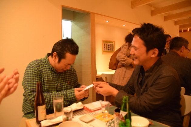 落語が終わった後、着替えてお客さんとビールを飲み交わす春風亭一蔵（左）とご祝儀を渡す常連客（右）