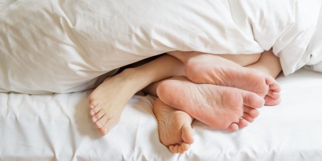 Two pairs of feet under the covers at home in bedroom