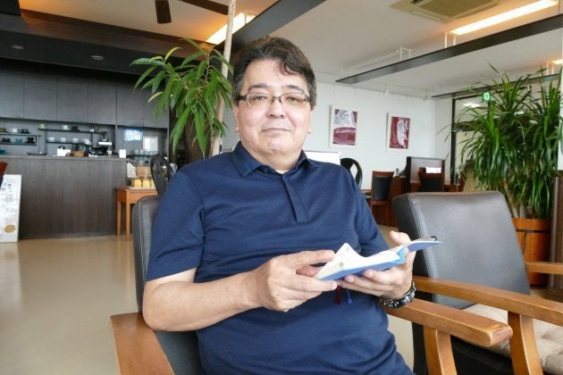 毎日の予定を書き込む手帳を手にクラウドファンディングへの挑戦について語る大庭英俊さん=うるま市与那城