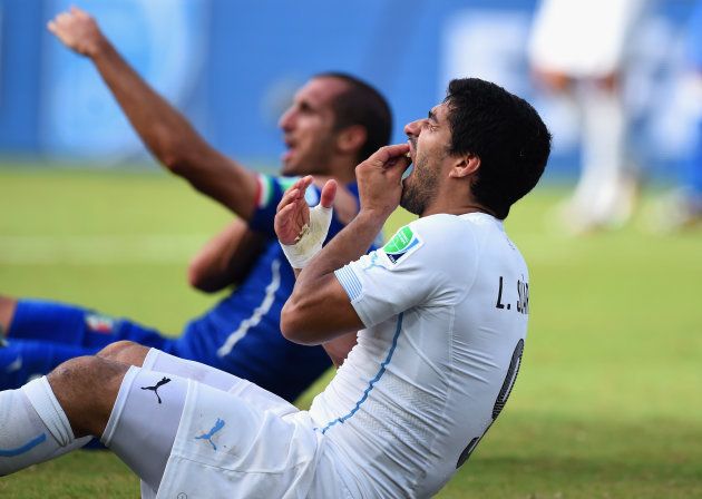 ワールドカップ・ブラジル大会で、イタリア選手（奥）に噛みついたにもかかわらず、自らが痛がる仕草をみせるウルグアイのスアレス＝2014年6月24日、ブラジル・ナタール