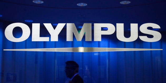 A man walks behind a logo of Japan's Olympus Corp at the company headquarters in Tokyo April 3, 2012. Japan's Olympus Corp may be able to recover from a $1.7 billion accounting fraud without raising capital, despite interest in an equity alliance from several investors including electronics giant Sony, Hiroyuki Sasa, its nominee president said on Tuesday. REUTERS/Yuriko Nakao (JAPAN - Tags: BUSINESS LOGO)