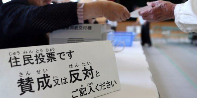 A resident (R) receives a ballot at a polling station in Osaka on May 17, 2015 to vote on a referendum to reform the city administration into a metropolitan government. The people of Osaka started voting on a plan to streamline Japan's second city in the mould of global metropolises like London, New York and Tokyo, as the one-time commercial capital seeks to recapture its glory days. JAPAN OUT -- AFP PHOTO / JIJI PRESS (Photo credit should read JIJI PRESS/AFP/Getty Images)