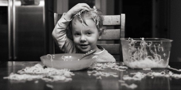 Silly toddler putting spaghetti on head at messy table