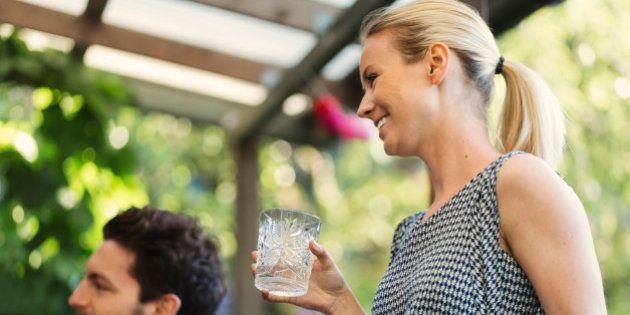 Happy woman holding glass while standing by friend at log cabin during summer party