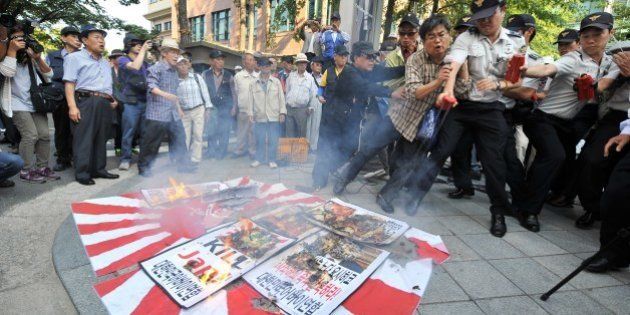 South Korean protestors burn a Japanese rising-sun flag and placards during an anti-Japanese rally over South Korean comfort women, outside the Japanese embassy in Seoul on September 24, 2012. Japan should resolve a long-standing grievance regarding Korean women forced to serve as sex slaves during World War II through a sincere apology and compensation, a senior Seoul official said on September 24, 2012, refuting published remarks on the matter by Japanese Prime Minister Yoshihiko Noda. AFP PHOTO/JUNG YEON-JE (Photo credit should read JUNG YEON-JE/AFP/GettyImages)