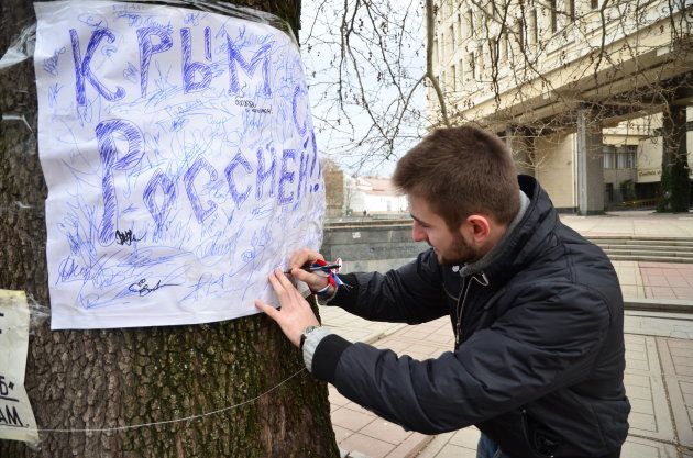 「クリミアよ、ロシアとともに」と書かれた旗に賛同の署名をする男性＝2014年3月、シンフェローポリ