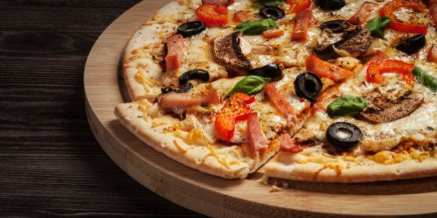 Letterbox panorama of sliced ham pizza with capsicum and olives on wooden board on table