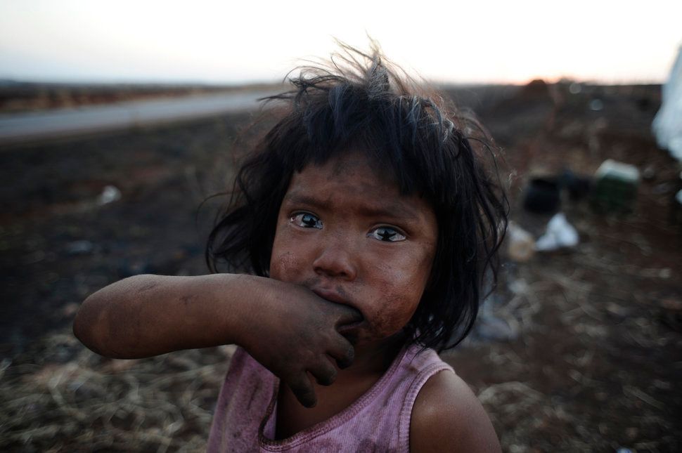 ブラジルのマトグロッソ・ド・スル州に暮らす先住民グラアニ＝カイオワ族の少女サンドリーリーさんが、正体不明の放火犯によって全焼した小屋の前に立つ。グラアニ＝カイオワ族は、先祖から伝わる土地の所有権をめぐって流血する衝突に巻き込まれている