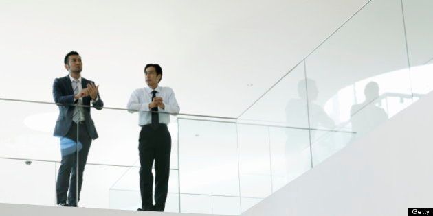 Businessman and mature businessman talking in office hallway resting arm on glass wall.Yokosuka Museum of Art,Kanagawa Prefecture,Japan.