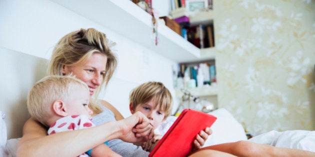 Mother with her sons watching tablet in bed