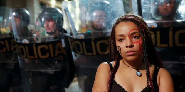 A woman with her face painted with the female gender symbol stands next to a police barricade during a protest against the gang rape of a 16-year-old girl in Sao Paulo, Brazil, Wednesday, June 1, 2016. In response to the assault, Brazil's interim President Michel Temer said that the country will set up a specialized group to fight violence against women. (AP Photo/Andre Penner)