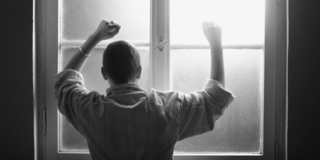 Young woman suffering from cancer leaning on the hospital window.