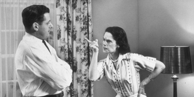 circa 1955: A woman gestures with her index finger as she scolds her husband, who stands with his arms folded in front of a window with drapes. She holds one hand on her hip. (Photo by Harold M. Lambert/Lambert/Getty Images)