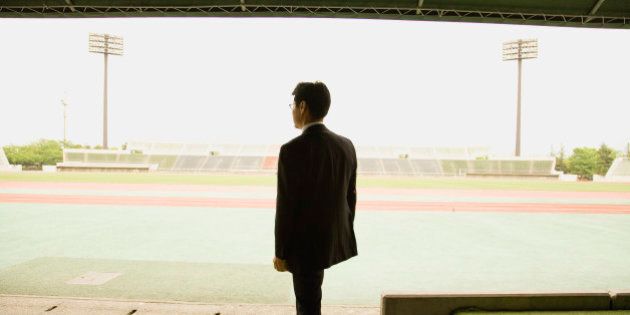 Soccer coach standing at stadium, rear view