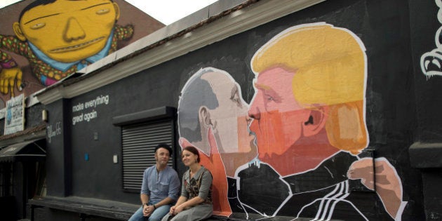 A couple sits in front of graffiti depicting Russian President Vladimir Putin, left, and Republican presidential candidate Donald Trump, on the walls of a bar in the old town in Vilnius, Lithuania, Saturday, May 14, 2016. (AP Photo/Mindaugas Kulbis)