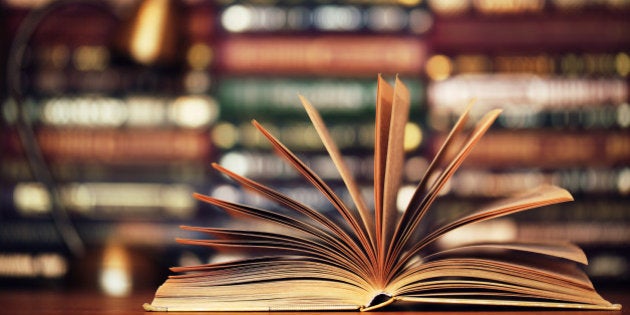 Open beautiful book laying on a table in a library. Angle-pose lamp in the background. Nice golden tones. Horizontal image. Color image. Tidy.