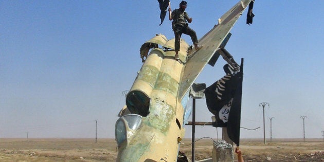 FILE - This undated image posted on Aug. 27, 2014 by the Raqqa Media Center of the Islamic State group, a Syrian opposition group, which has been verified and is consistent with other AP reporting, shows fighters of the Islamic State group waving the group's flag from a damaged display of a government fighter jet following the battle for the Tabqa air base, in Raqqa, Syria. The Islamic State group is test flying, with the help of former Iraqi air force pilots, several fighter jets captured earlier from air bases belonging to the Syrian military, a Syrian activist group said Friday, Oct. 17, 2014. The report by the Britain-based Syrian Observatory for Human Rights could not be independently confirmed, and U.S. official said they had no reports of Islamic State group militants flying jets in support of their forces on the ground.(AP Photo/ Raqqa Media Center of the Islamic State group)