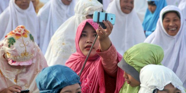 An Indonesian Muslim woman adjusts a selfie stick as she prepares to take a selfie during Eid al-Fitr prayer that marks the end of the holy fasting month of Ramadan on Parang Kusumo Beach in Yogyakarta, Indonesia, Monday, July 28, 2014. (AP Photo/Slamet Riyadi)
