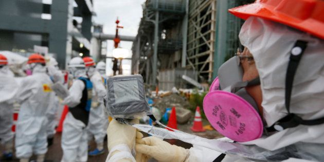 A worker wearing protective clothing and mask measures the radiation in the air as employees prepare materials used to create a frozen underground wall to surround the crippled reactor buildings at Tokyo Electric Power Co.'s (Tepco) Fukushima Dai-ichi nuclear power plant in Okuma, Fukushima Prefecture, Japan, on Wednesday, July 9, 2014. All of Japan's 48 operable commercial reactors are idled for safety assessments after the accident at the Fukushima plant. Photographer: Kimimasa Mayama/Pool via Bloomberg